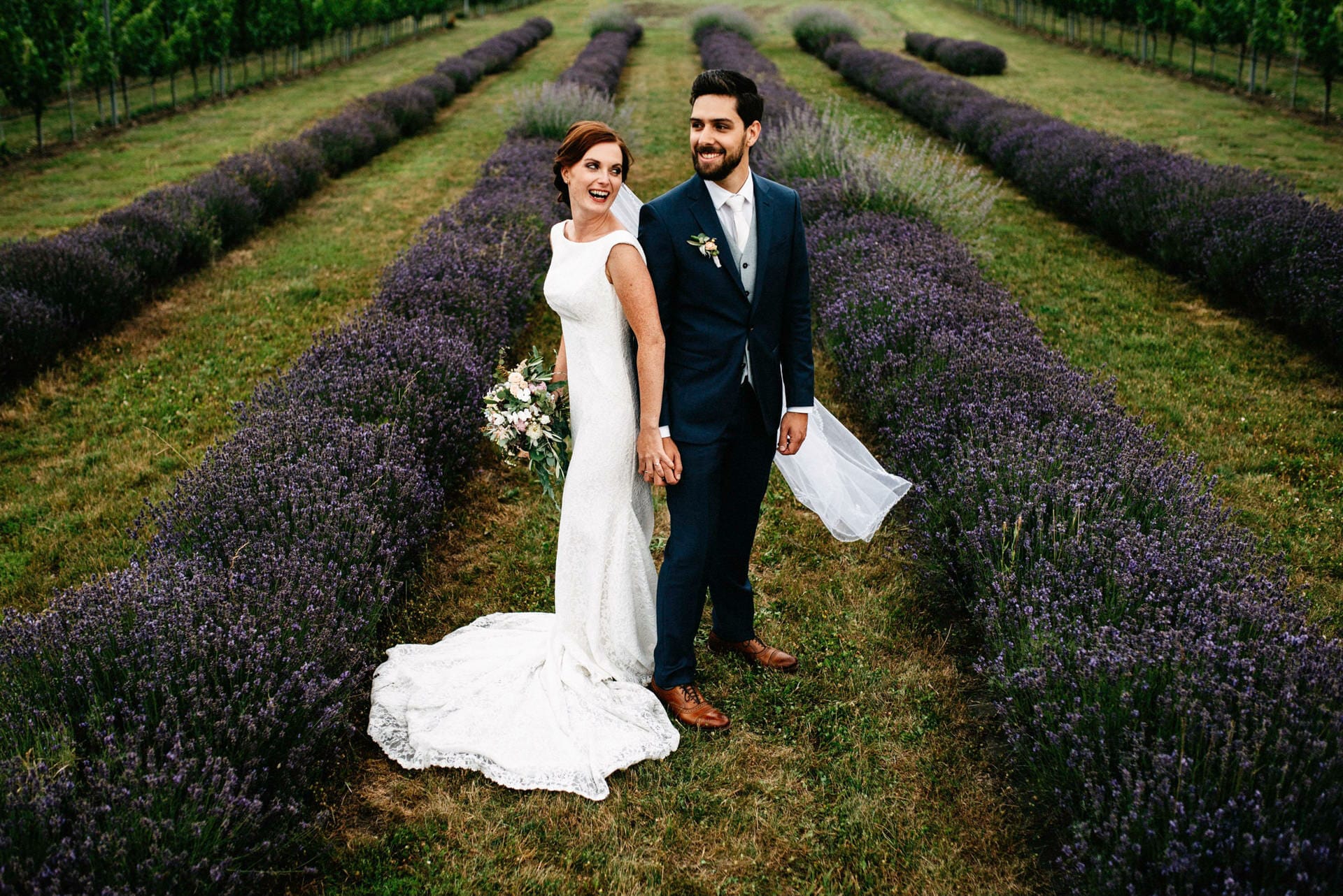 Hochzeitspaar steht im Lavendelfeld in der Steiermark und sieht sich verliebt an. Braut hat Brautstrauß in der Hand.