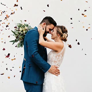 Glücklicher Moment zwischen Brautpaar während Blumen auf sie fliegen